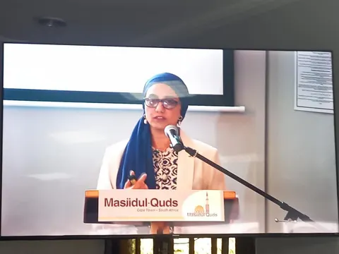 Rumana Mahomed speaking at a Masjidul-Quds lectern, shown on a large screen